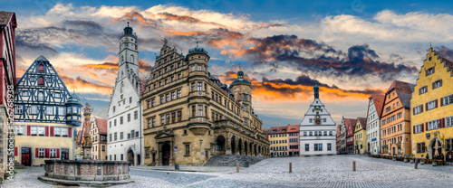 Die Fassade des Rathauses, der Ratsherrntrinkstube und anderer Gebäude rahmen den historischen Marktplatz der Altstadt von Rothenburg ob der Tauber in der Dämmerung ein, bei stimmungsvollem Himmel