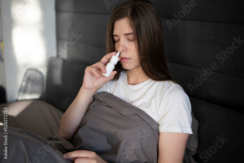Sick woman lies in bed atient shoves a spray into the nose to treat rhinitis, an allergy with difficulty breathing. Treatment of the disease. Concept: illness: Rhinitis, sinusitis, cold, flu