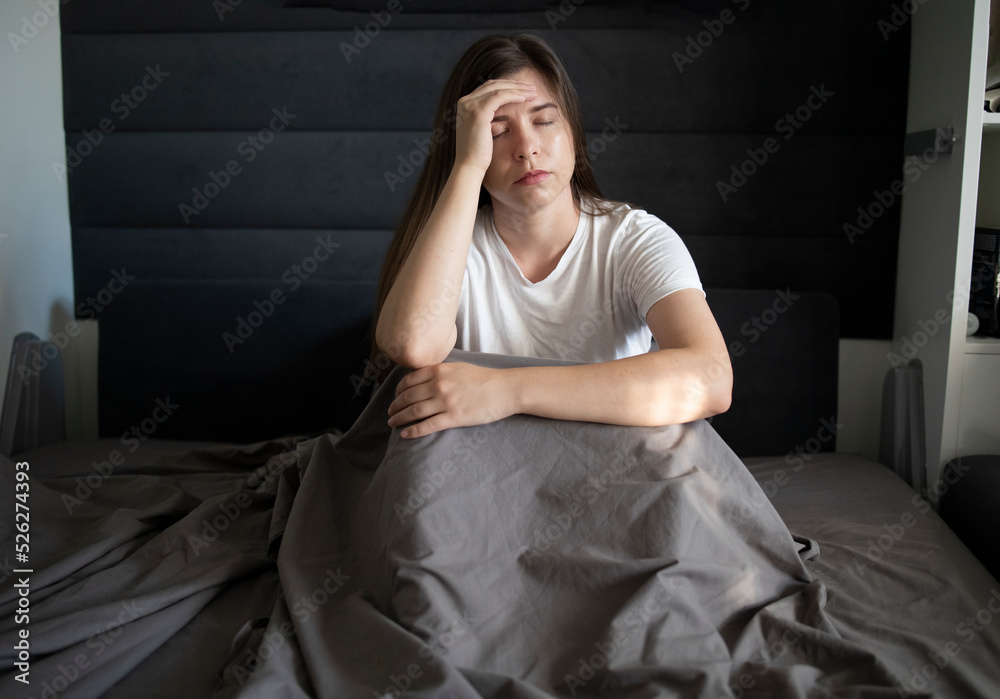 Young woman is lying in bed and holding her head with her hands, experiencing a headache, migraine. Concept: sleep disorders caused by stress, anxiety and problems Young woman is lying in bed and holding her head with her hands, experiencing a headache, migraine. Concept: sleep disorders caused by stress, anxiety and problems