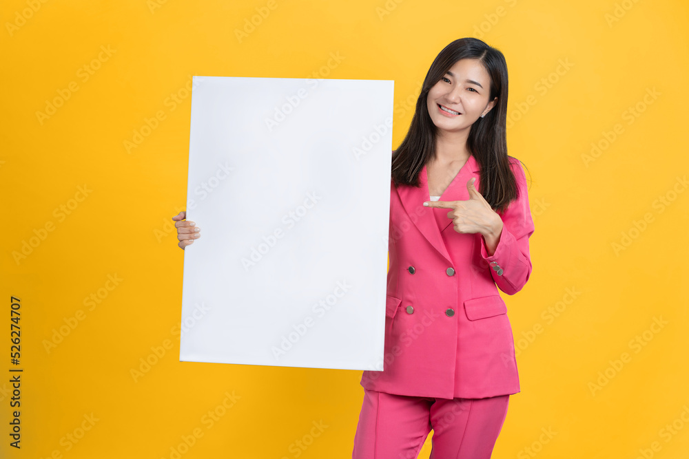 Cheerful Young Asian businesswoman is standing behind the white blank banner or empty copy space advertisement board on background, Looking at camera Cheerful Young Asian businesswoman is standing behind the white blank banner or empty copy space advertisement board on background, Looking at camera