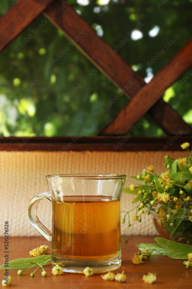 Glass cup of aromatic tea and linden blossoms on wooden table, space for text Glass cup of aromatic tea and linden blossoms on wooden table, space for text