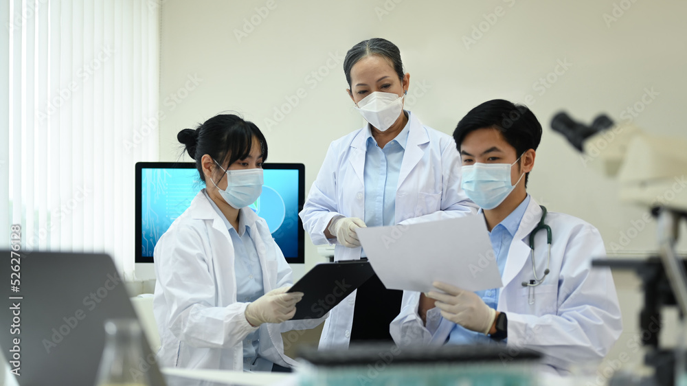 Team of young research scientists and senior supervisor discussing about new test results, working together in laboratory Team of young research scientists and senior supervisor discussing about new test results, working together in laboratory