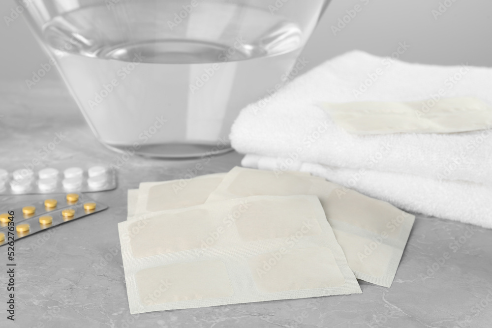 Fototapeta premium Mustard plasters, pills, towel and bowl with water on light grey marble table, closeup