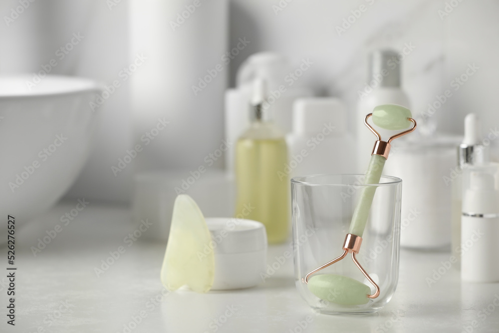 Natural face roller, gua sha tool and cosmetic products on counter in bathroom. Space for text Natural face roller, gua sha tool and cosmetic products on counter in bathroom. Space for text