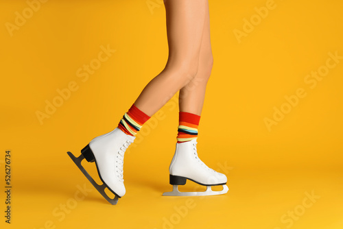 Woman in elegant white ice skates on yellow background, closeup of legs