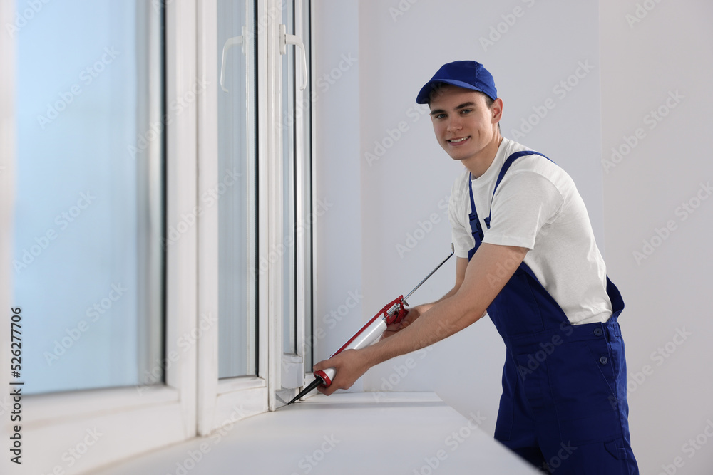 Worker sealing plastic window with caulk indoors. Installation process Worker sealing plastic window with caulk indoors. Installation process