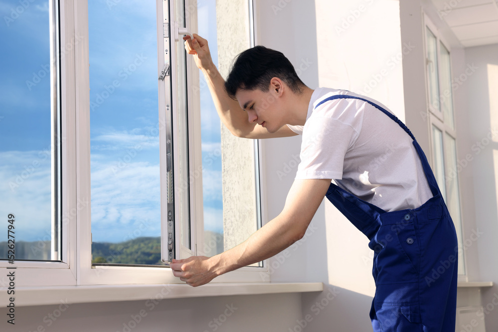 Worker in uniform installing plastic window indoors Worker in uniform installing plastic window indoors