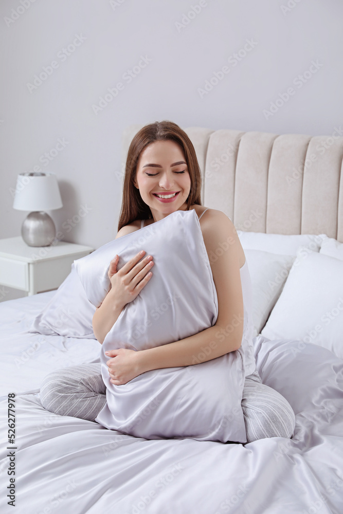 Young woman hugging pillow on comfortable bed with silky linens Young woman hugging pillow on comfortable bed with silky linens