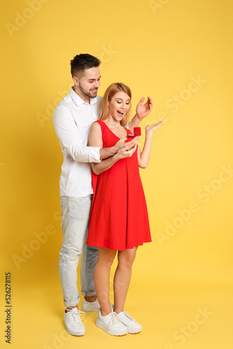 Man with engagement ring making marriage proposal to girlfriend on yellow background