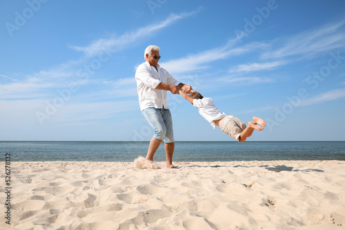 Cute little boy with grandfather having fun on sea beach