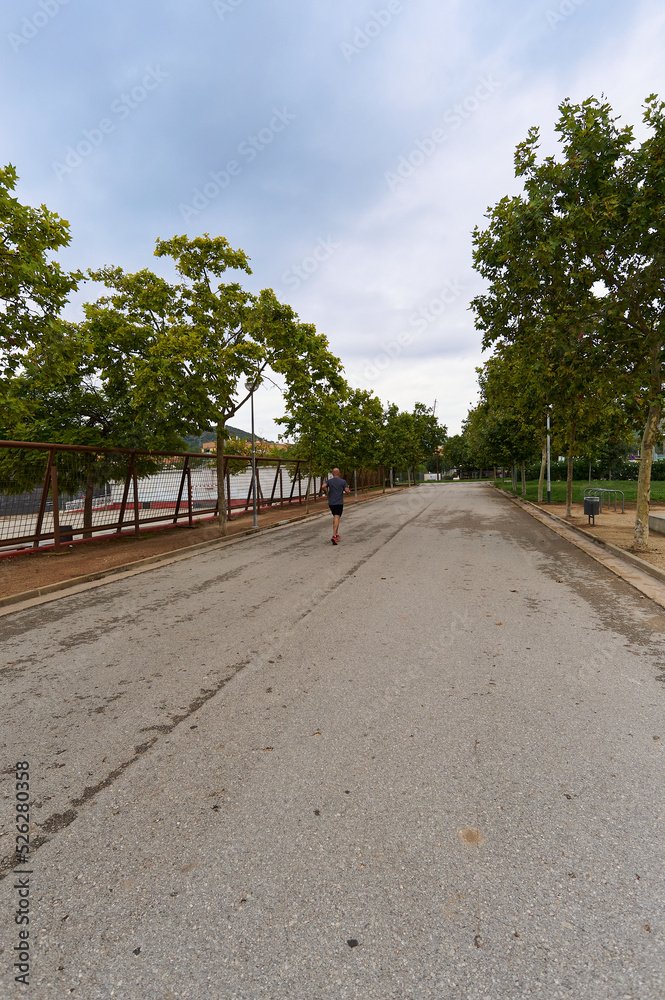 Person running alone on the asphalt in the empty park surrounded by trees. Person running alone on the asphalt in the empty park surrounded by trees.