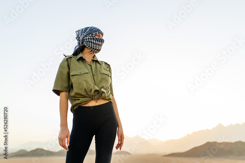 woman with covered head and face with black and white checkered scarf standing desert background