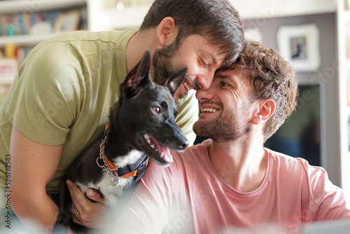 Close up of happy gay couple with dog adopted at animal shelter - Portrait of young man with pet while kissing his husband