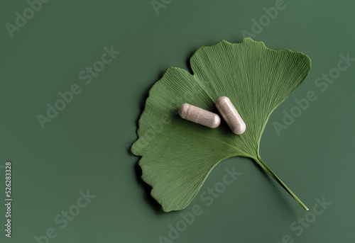 Ginkgo leaf with pills for brain, memory protect therapy and treatment of dementia. Ginkgo Biloba composition on green background, natural ingredient for alternative medicine, top view.