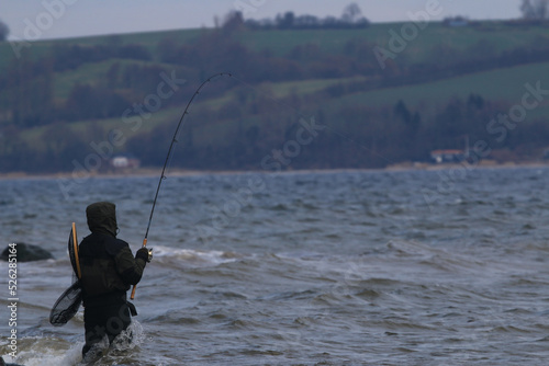 Angler in waders in drilling action with a hooked fish.