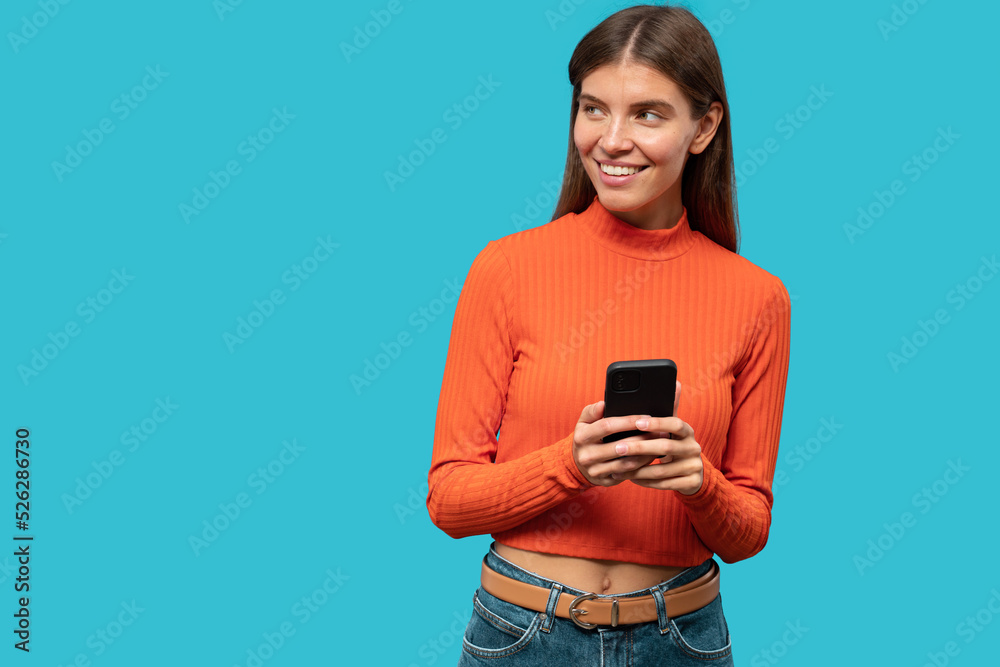 Portrait of woman testing dating app on phone on blue studio background looking on copy space