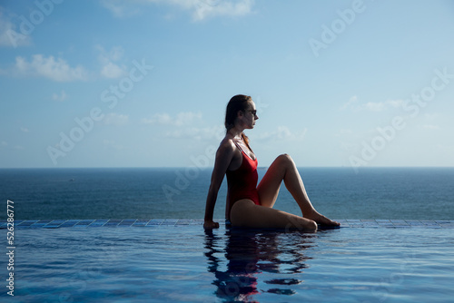 Young woman in a red swimsuit sits on the edge of the pool