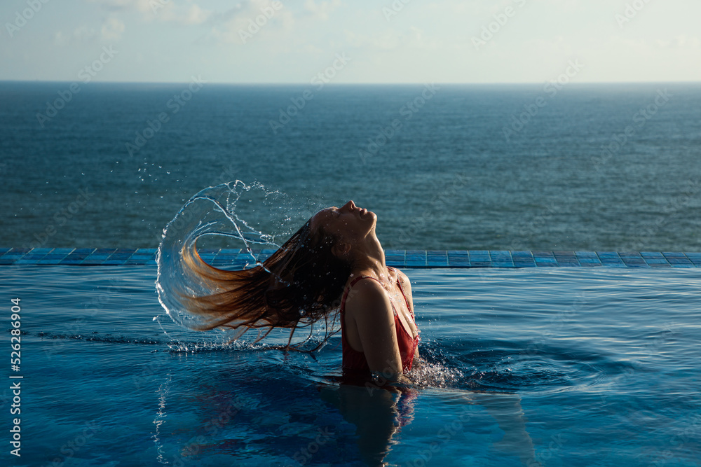 Naklejka premium Young woman in red swimsuit tossing hair out of the water