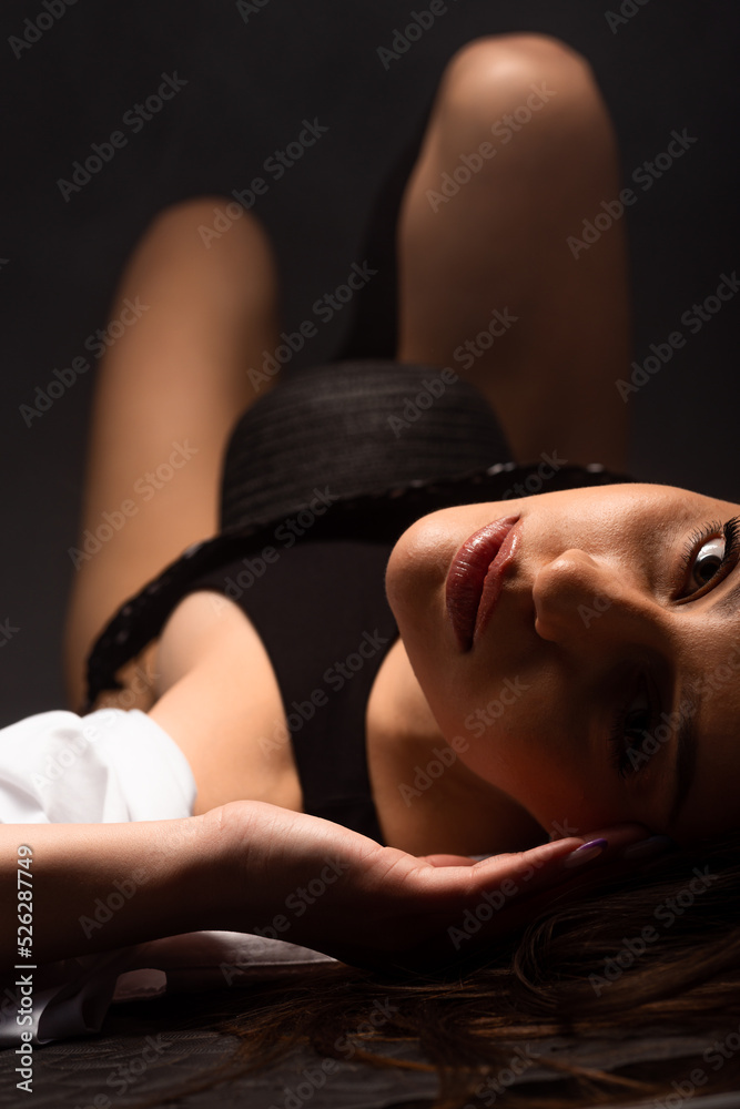 Obraz premium Portrait of young sensual slim dark haired woman in black bodysuit lying on floor