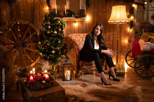 smiling beautiful business woman with mobile phone sitting on a christmas chair in moody set waiting
