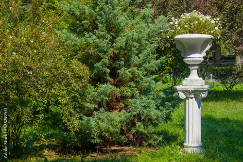 Large white ceramic vase with flowers on a column in the garden on a sunny summer day