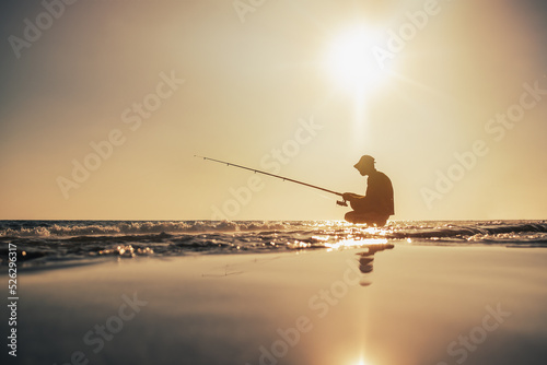 Fishermen silhouette fishing on the seashore in the evening under warm sun photo