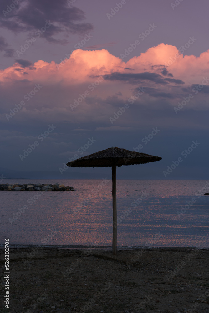 beach umbrella after a storm during sunset with calm sea and warm colors beach umbrella after a storm during sunset with calm sea and warm colors
