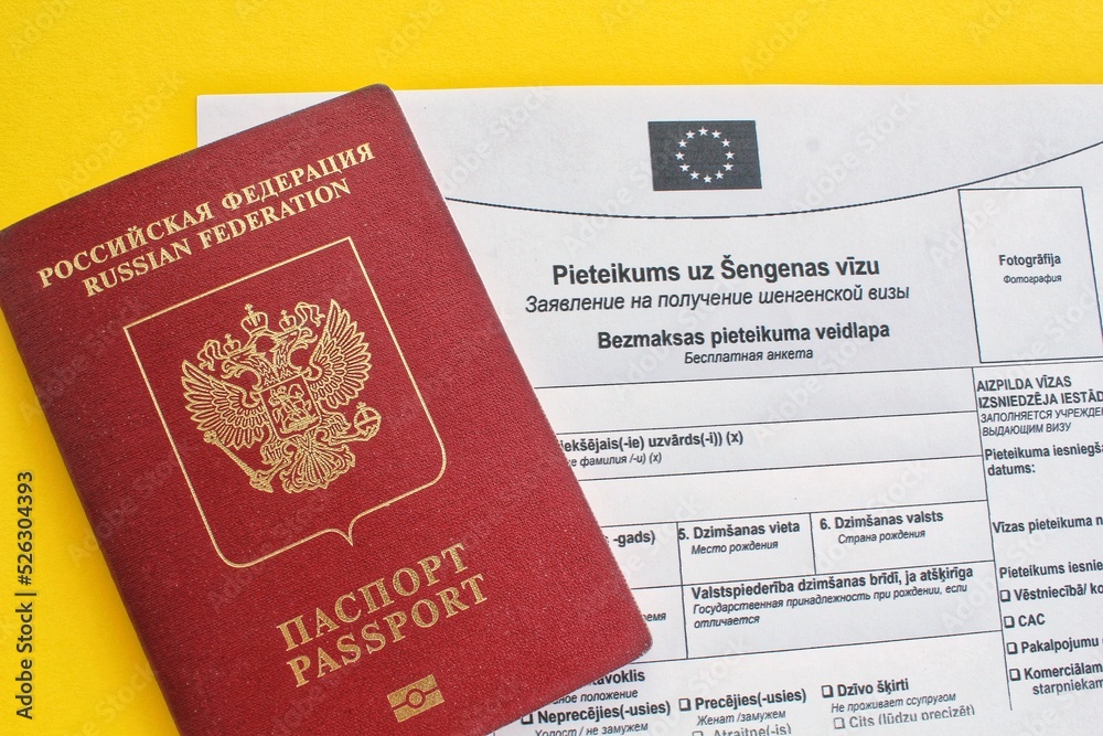 Fototapeta premium Schengen visa application form in Russian and Latvian language and passport on yellow background. Prohibition and suspension of visas for tourists to travel to European Union and Baltic States concept