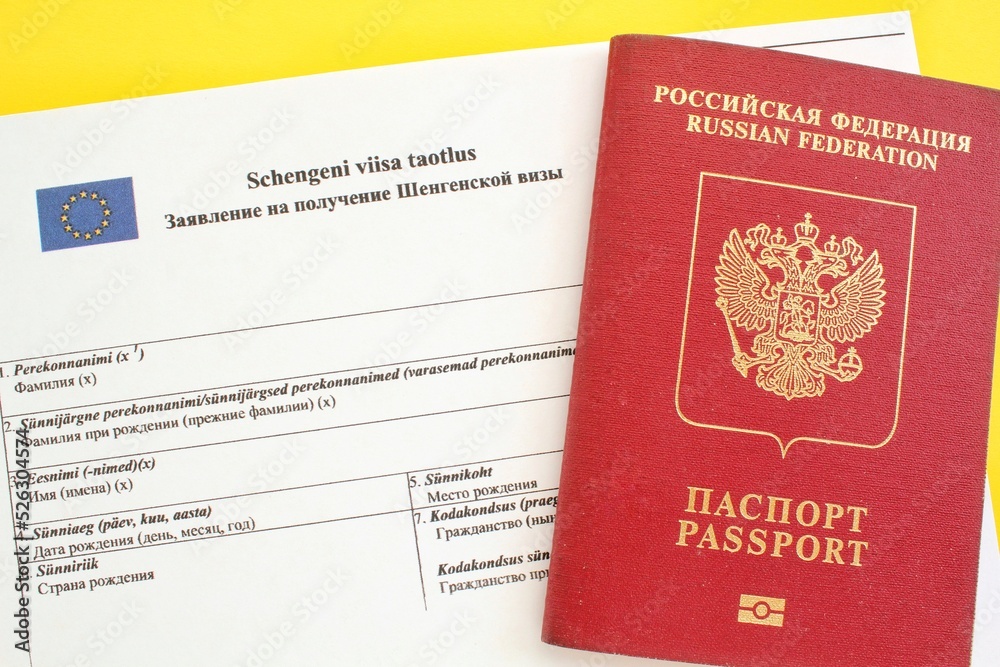 Schengen visa application form in Russian and Estonian language and passport on yellow background. Prohibition and suspension of visa for Russian tourists to travel to European Union and Baltic States Schengen visa application form in Russian and Estonian language and passport on yellow background. Prohibition and suspension of visa for Russian tourists to travel to European Union and Baltic States