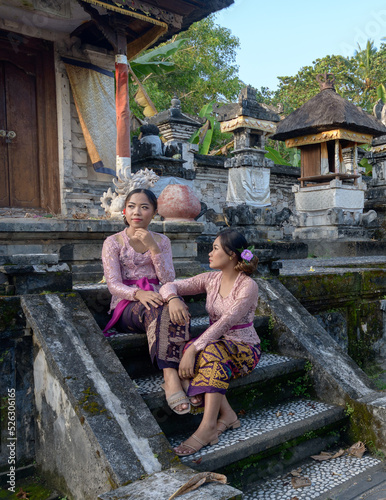 Portrait two Bali girls in colorful traditional clothes on the steps in old temple. photo