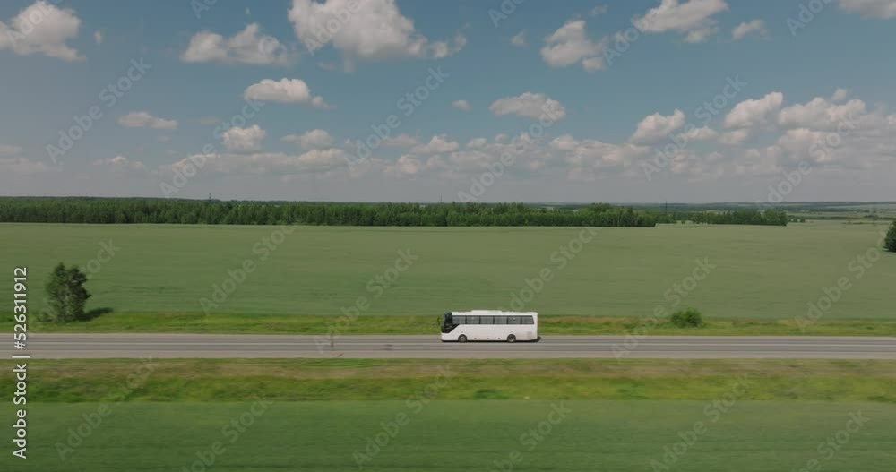 Travel tour bus driving alone on straight highway through plain field. White bus fast speed moving on freeway. Aerial drone wide shot at summer sunny day. Travel tour bus driving alone on straight highway through plain field. White bus fast speed moving on freeway. Aerial drone wide shot at summer sunny day.