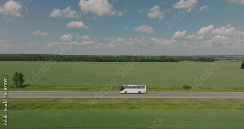 Travel tour bus driving alone on straight highway through plain field. White bus fast speed moving on freeway. Aerial drone wide shot at summer sunny day.