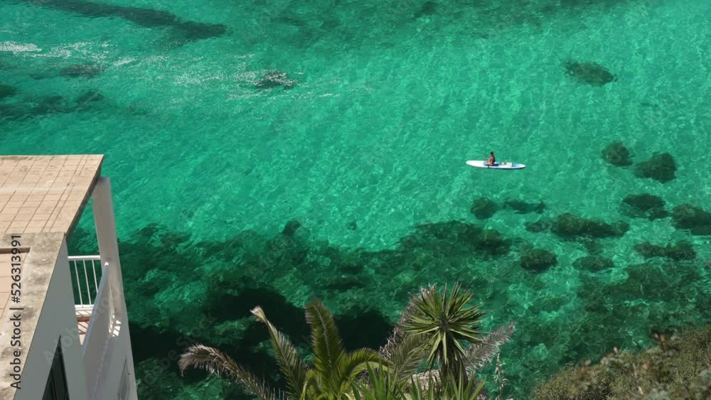 Paddle boarder on turquoise water from elevated position at Cala en Porter, Menorca, Balearic Islands