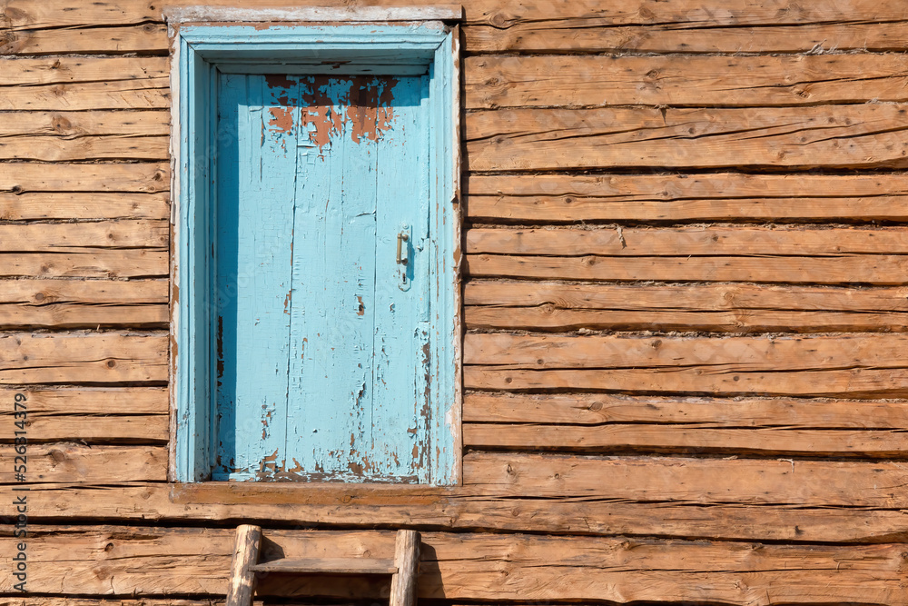 Wall of an old village house made of logs during renovation. There is an old door with peeling blue paint and a small ladder. Background. Concept. Wall of an old village house made of logs during renovation. There is an old door with peeling blue paint and a small ladder. Background. Concept.