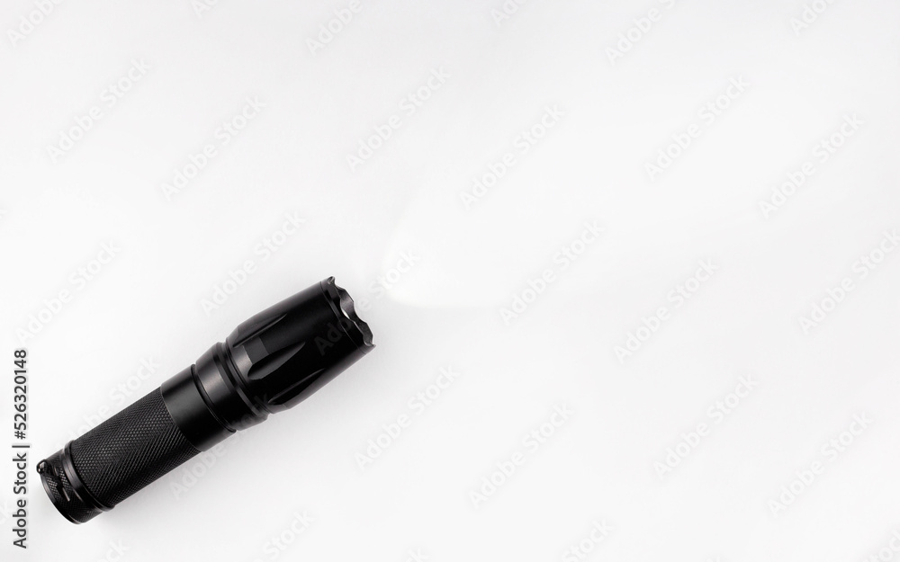 A black metal flashlight shines on a white background. Copy space. Concept