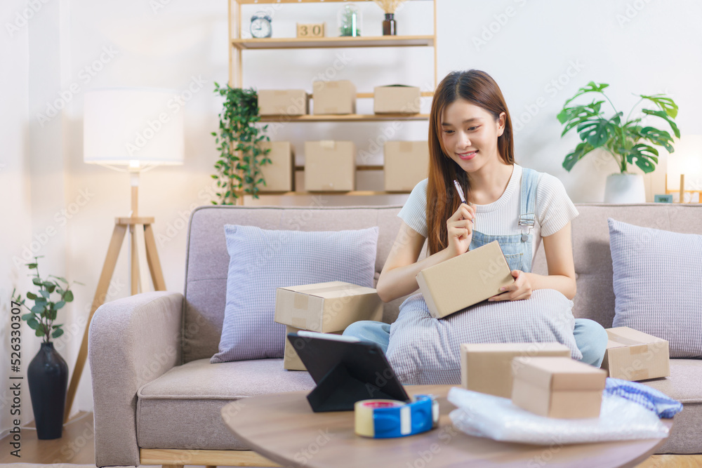 Online trader concept, Female entrepreneur look data on tablet and write address on parcel boxes Online trader concept, Female entrepreneur look data on tablet and write address on parcel boxes