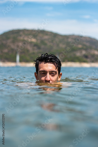 Handsome Caucasian man submerged in water. He is on a beach and you can only see his eyes and his hair is wet © JuanDiego