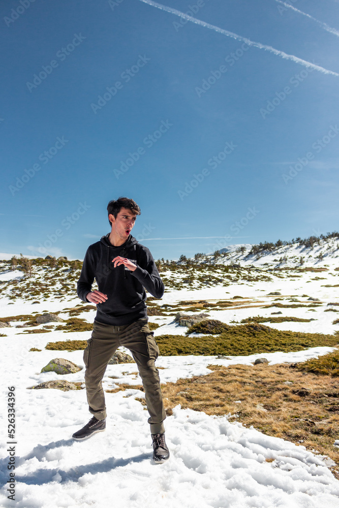 Caucasian handsome man fighting in the middle of a snowy place. He is wearing a black sweeter