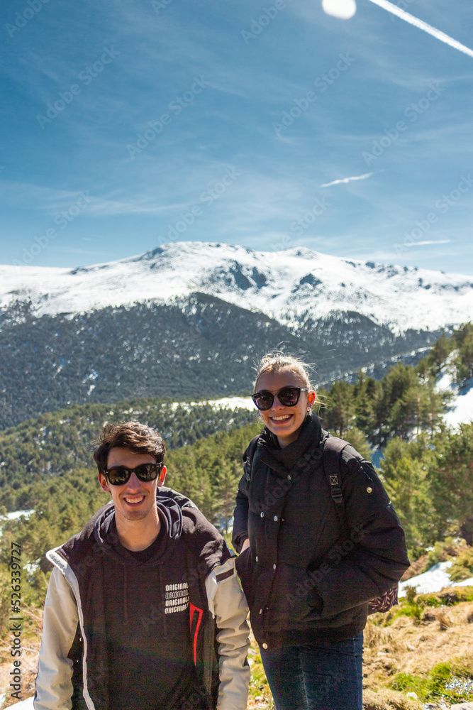 Beautiful friends with sun glasses posing in the middle of a snowy of a pine forest. They are smiling