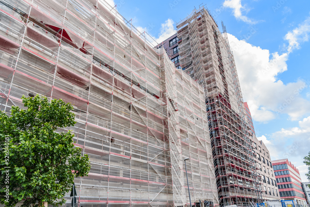Low angle view of a high rise building in construction with wrapped scaffolding under blue sky with clouds