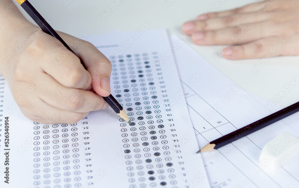 Students hand holding pencil writing selected choice on answer sheets and Mathematics question sheets. students testing doing examination. school exam Students hand holding pencil writing selected choice on answer sheets and Mathematics question sheets. students testing doing examination. school exam