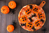 Halloween jack o lantern pizza. Top down view table scene on a dark wood background with pumpkins.