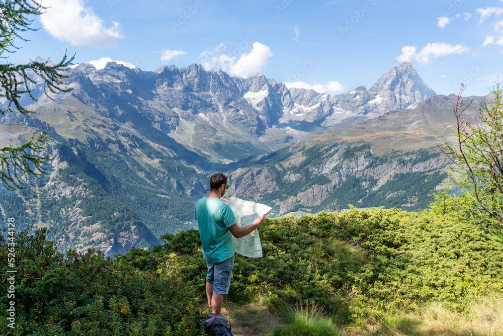 Standing man looking a map during a hiking day at Aosta Valley in italian alps. Active vacations around Matterhorn. 