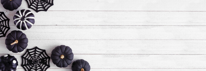 Halloween corner border of black and white patterned pumpkins and spider web decor. Above view on a white wood banner background. Copy space.