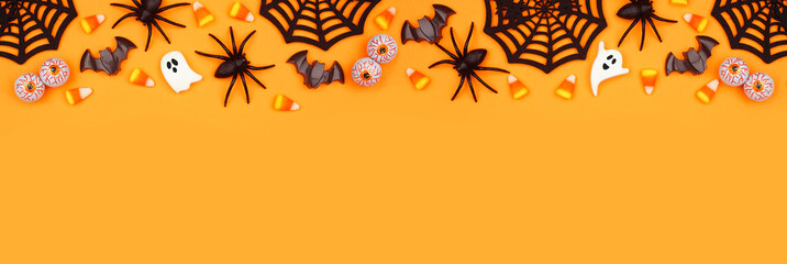 Halloween top border of scattered candy and decor. Above view over an orange banner background with copy space.
