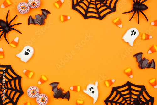 Halloween frame of scattered candy and decor. Top down view over an orange background with copy space. #526344706