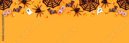 Halloween top border of scattered candy and decor. Above view over an orange banner background with copy space. #526344707