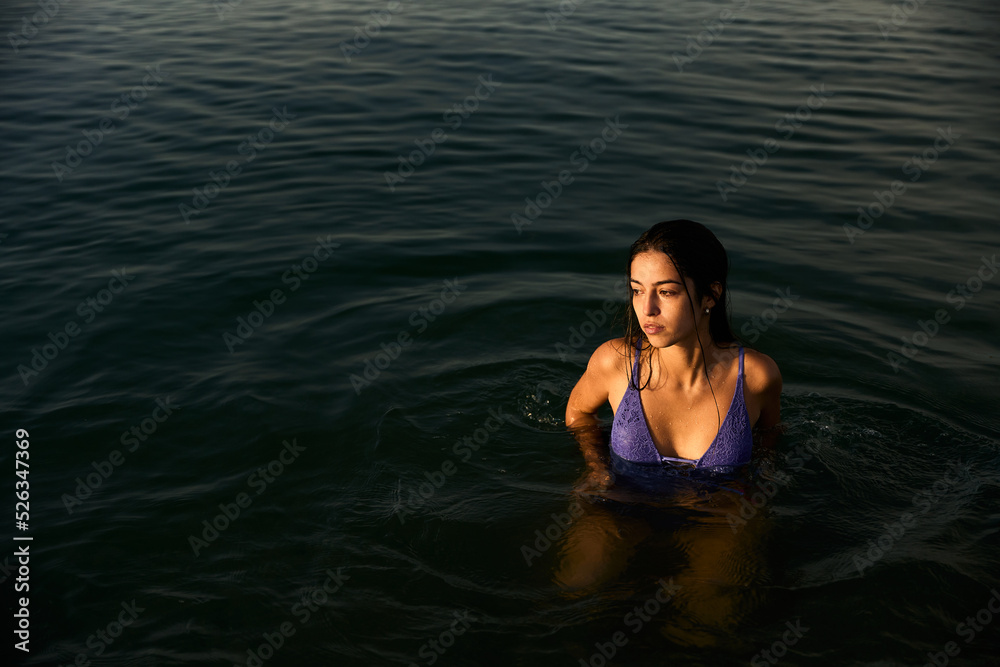 young girl wearing a purple swimming suite taking a morning bath on the mediterranean sea at the sunrise in a warm summer day