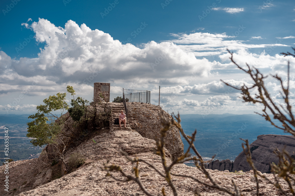 Shot of female hiker on top of Montserrat mountain in Spain. Traveler woman sitting on a stone looking at the view.