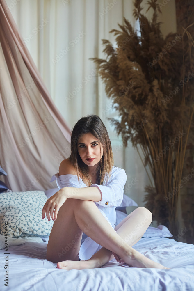 A girl in black underwear and a white shirt is lying on a bed in a loft-style interior. A girl in black underwear and a white shirt is lying on a bed in a loft-style interior.